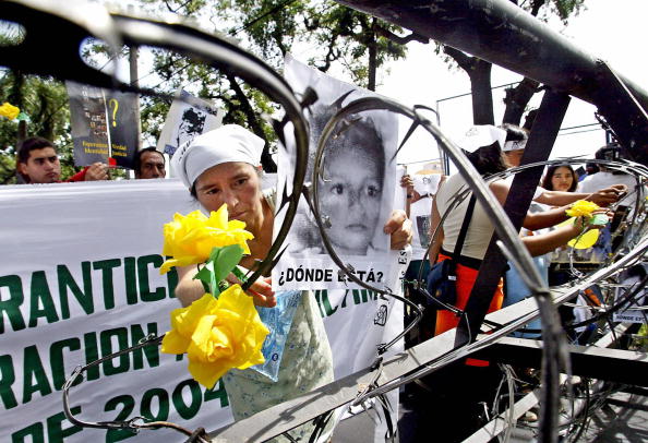 A Salvadorian mother lifts a portrait of her son near the Presidential House as part of a rally of relatives who lost their children during military operations in the last civil war (1980-1992) in San Salvador, El Salvador. NGO Pro-Busqueda has been working in the search of about 473 missing children (Photo Credit: Yuri Cortez/AFP/Getty Images).