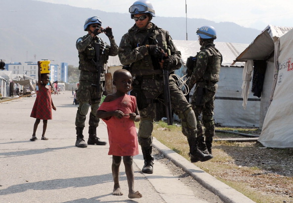 Brazilian soldiers patrol a camp for survivors of the January 2010 quake in Haiti. Hundreds of thousands are still living rough in squalid makeshift camps, and they now face rampant crime, a cholera outbreak and the occasional hurricane (Photo Credit: Vanderlei Almeida/AFP/Getty Images).
