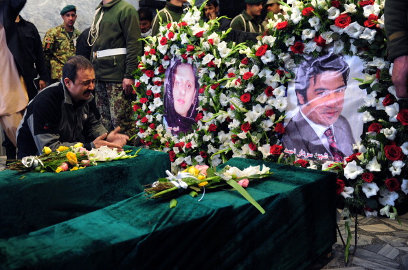 The nephew of slain Afghan AFP reporter Sardar Ahmad laments over the coffins of two of Sardar's children alongside images of Sardar's wife and Sardar during funeral ceremonies on March 23, 2014 (Photo Credit: Roberto Schmidt/AFP/Getty Images).