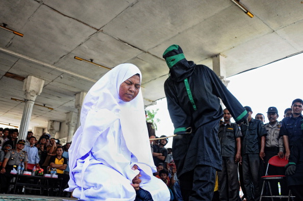 A crowd watches as a woman is caned by a sharia police officer dressed in black robes at a public square in Aceh, Indonesia's only province that practices partial sharia law (Photo Credit: Riza Lazuardi/AFP/Getty Images).