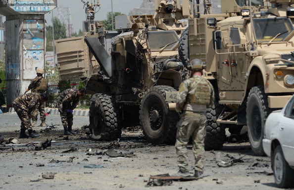 U.S. soldiers part of NATO-led International Security Assistance force (ISAF) and Afghan security forces inspect the wreckage of an armored vehicle at the site of a suicide attack in Kabul on August 10, 2014. Photo credit: Shah Marai/AFP/Getty Images)