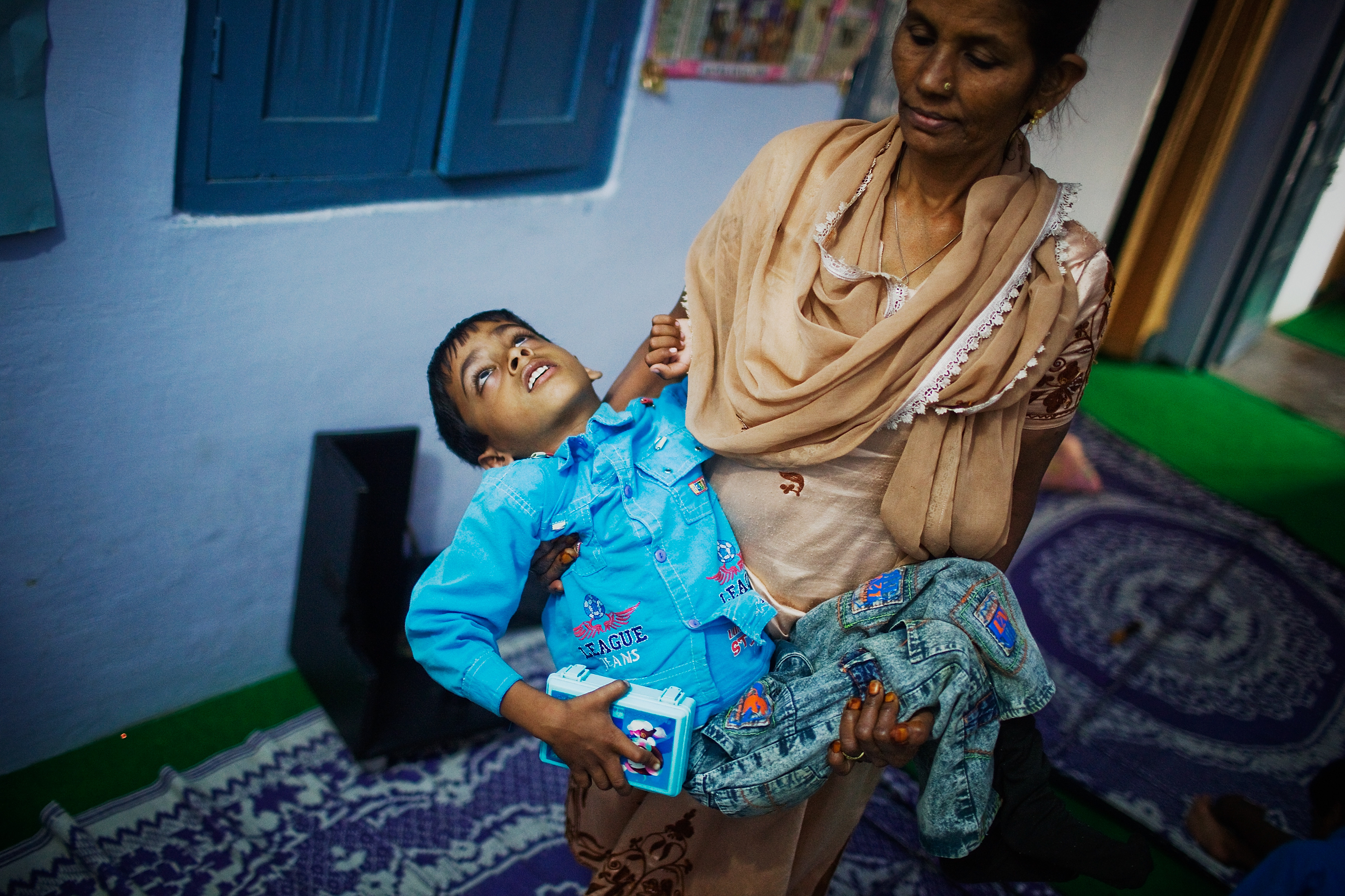 8 year old Annan is carried by Nafiza Bee co-ordinator of the Chingari Trust clinic in Bhopal, India. Twenty-five years after an explosion causing a mass gas leak, in the Union Carbide factory in Bhopal, killed at least eight thousand people. A new generation is growing up sick, disabled and struggling for justice. (Photo by Daniel Berehulak/Getty Images)