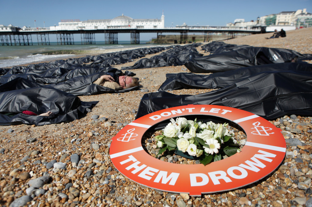 SOS Europe - Die-in, Brighton Beach, England. Photo shows people lying on Brighton beach ( Brighton Pier in the background ) in black body bags. A life saving ring on the pebbles reads ' Don't Let Them Drown.  Brighton beach was covered in 200 body bags as Amnesty International volunteers raised awareness of the plight of thousands of migrants ahead of emergency EU talks on 23rd April 2015. Local Amnesty members and volunteers zipped themselves into some of the body bags at around 10am, alongside a banner saying #DontLetThemDrown. Campaigners hope the protest, organised ahead of an EU meeting on the mounting death toll in the Mediterranean seas, will highlight the UK?s ?shameful? response to the crisis.