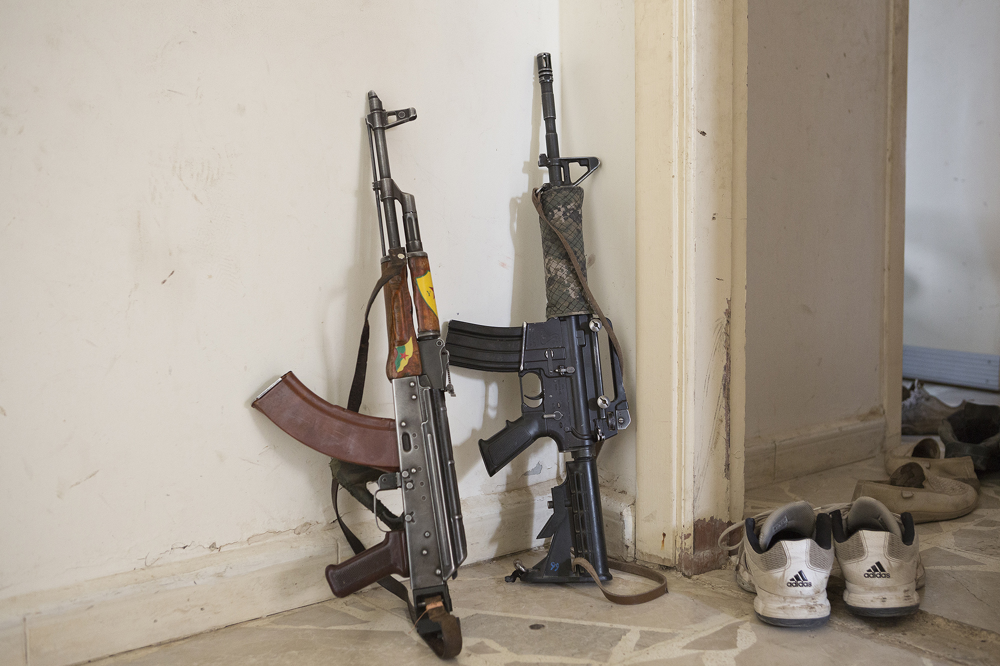 28/09/2014. Al-Yarubiyah, Syria. A Chinese made Kalashnikov and American M4 rifle (the latter captured from ISIS militants) lean against a wall in a building occupied by Syrian Kurdish YPG fighters in Al-Yarubiyah, Syria.
