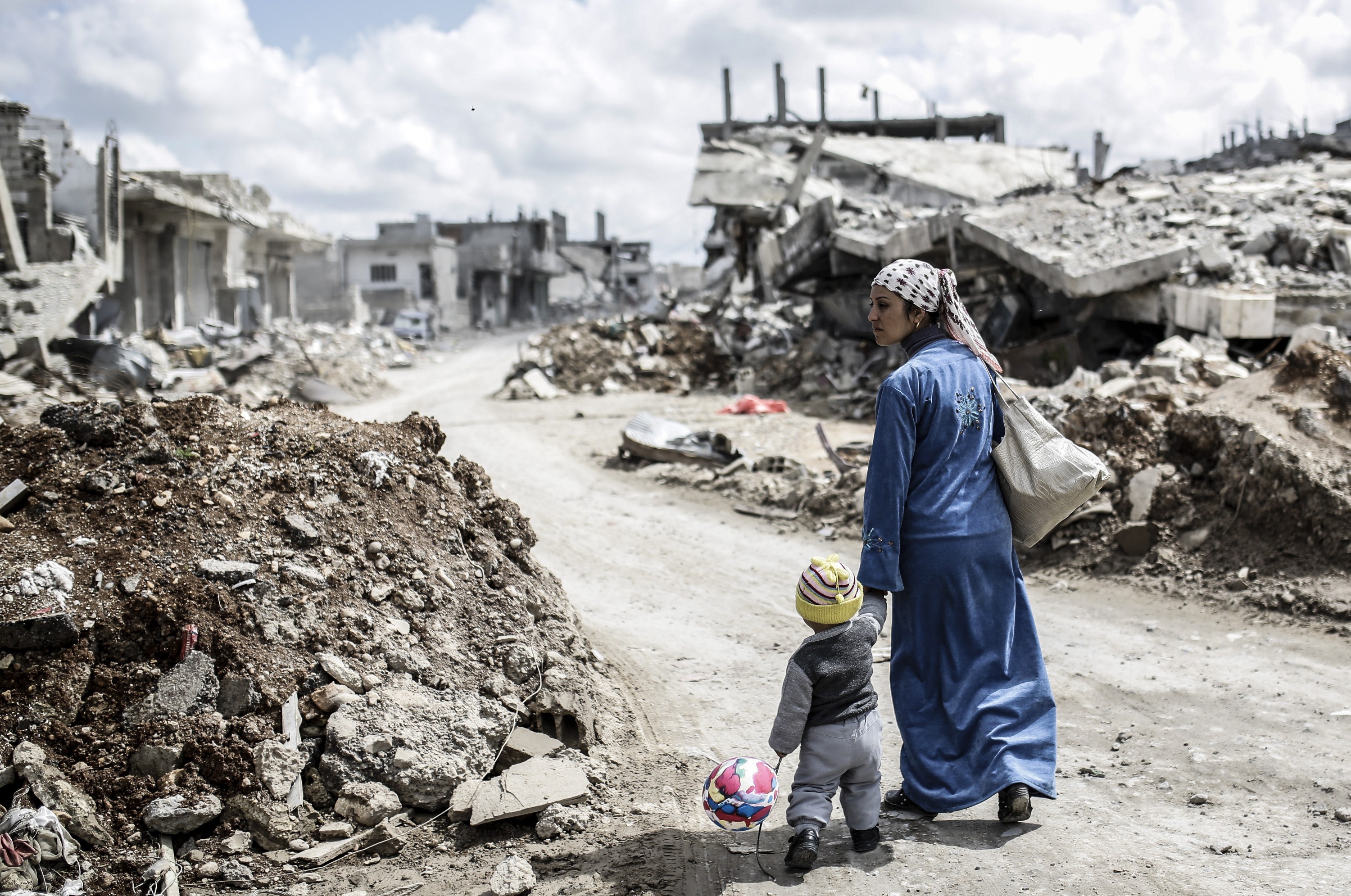 A Kurdish Syrian woman walks with her child past the ruins of the town of Kobane, also known as Ain al-Arab, on March 25, 2015. Islamic State (IS) fighters were driven out of Kobane on January 26 by Kurdish and allied forces. AFP PHOTO/YASIN AKGUL        (Photo credit should read YASIN AKGUL/AFP/Getty Images)