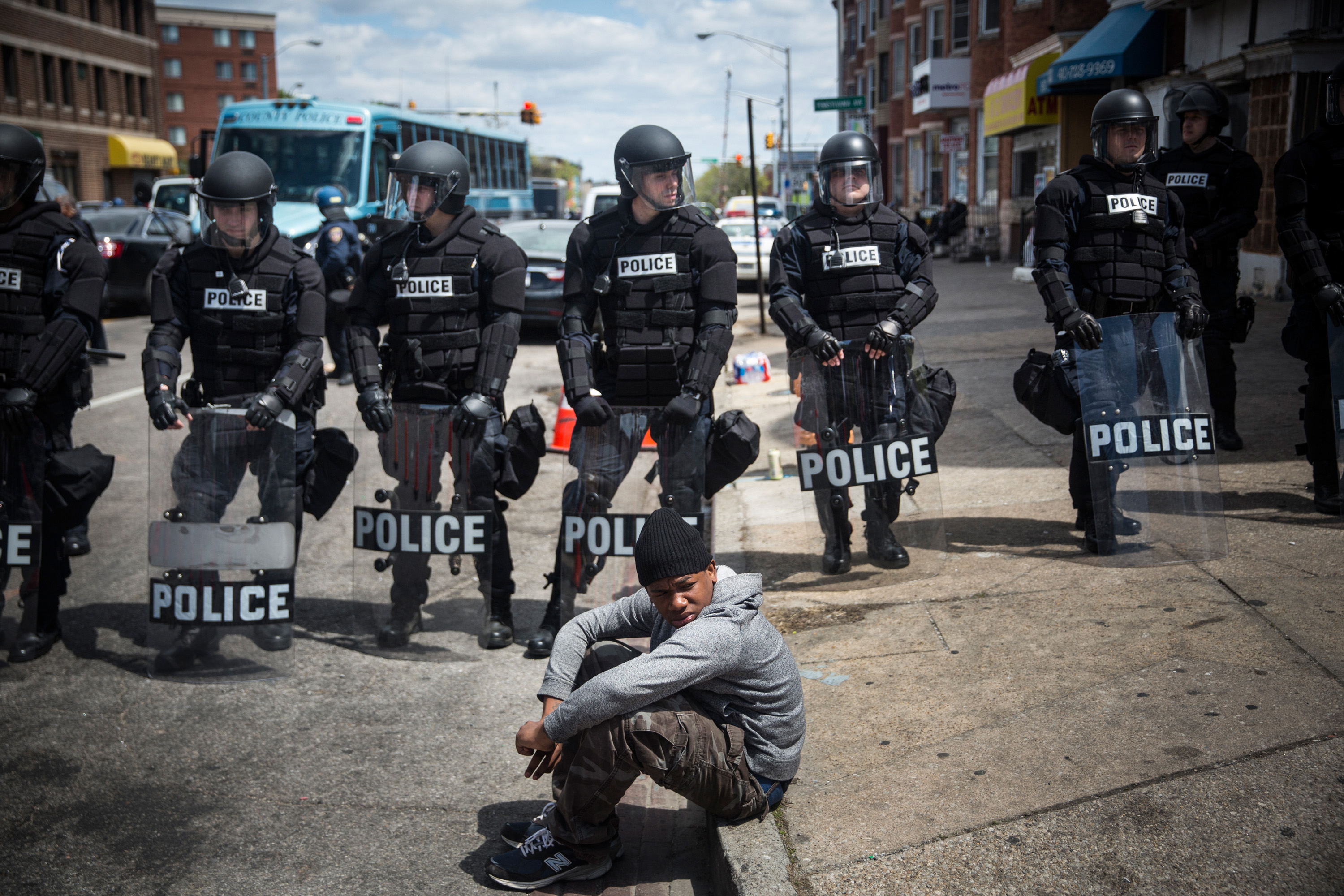 BALTIMORE, MD - APRIL 28: Daquan Green, age 17, sits on the curb while riot police stand guard near the CVS pharmacy that was set on fire yesterday during rioting after the funeral of Freddie Gray, on April 28, 2015 in Baltimore, Maryland. Gray, 25, was arrested for possessing a switch blade knife April 12 outside the Gilmor Houses housing project on Baltimore's west side. According to his attorney, Gray died a week later in the hospital from a severe spinal cord injury he received while in police custody. (Photo by Andrew Burton/Getty Images)