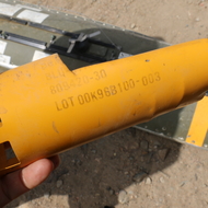 Part of a US-made CBU-87 cluster bomb (in background) and fragment of BLU-97 cluster sub-munitions (in hand) dropped by Saudi-led coalition forces in the centre of al-Magash, a village west of Sa’da City.
